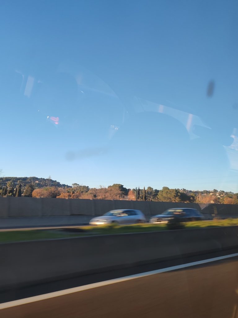 Vista di un'autostrada con traffico, alberi verdi e cielo terso in lontananza.